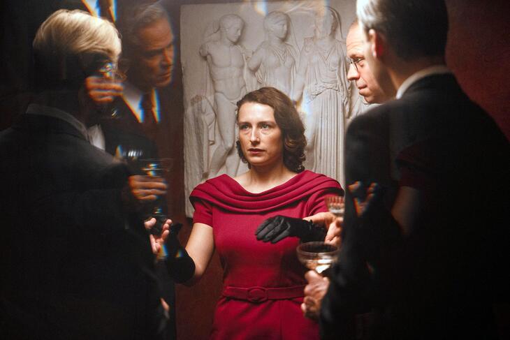 Una mujer vestida de rojo rodeada de varios hombres, en un fotograma de Woman Unknown.