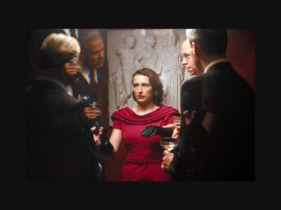 Una mujer vestida de rojo rodeada de hombres, en Woman Unknown.