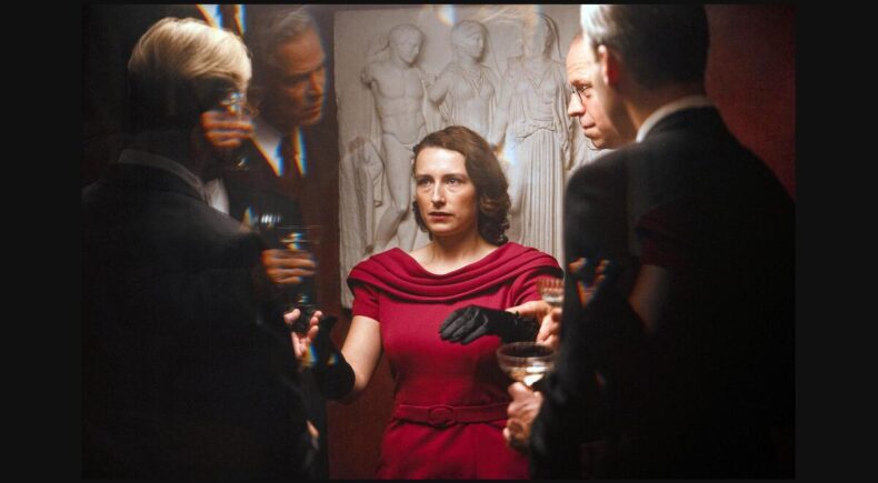 Una mujer vestida de rojo rodeada de hombres, en Woman Unknown.